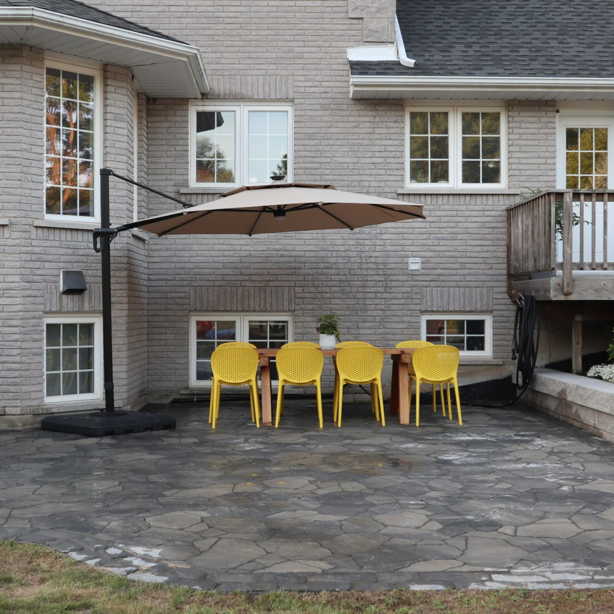 Permacon Rosebel patio with a cedar harvest table surrounded by yellow economy outdoor chairs in Woodstock